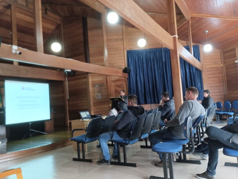a foto foi tirada nas dependências da Câmara Municipal, e mostra o público que assiste à audiência, e o Prefeito Municiapal fazendo sua explanação.